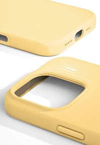 Gele telefoonhoes van mat siliconen, met uitsparingen voor camera en poorten, met de tekst "IDEAL OF SWEDEN" aan de zijkant.