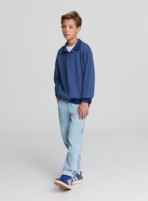 Maglione blu con collo, abbinato a jeans azzurri e sneakers blu con strisce bianche. Tessuto liscio, vestibilità comoda.