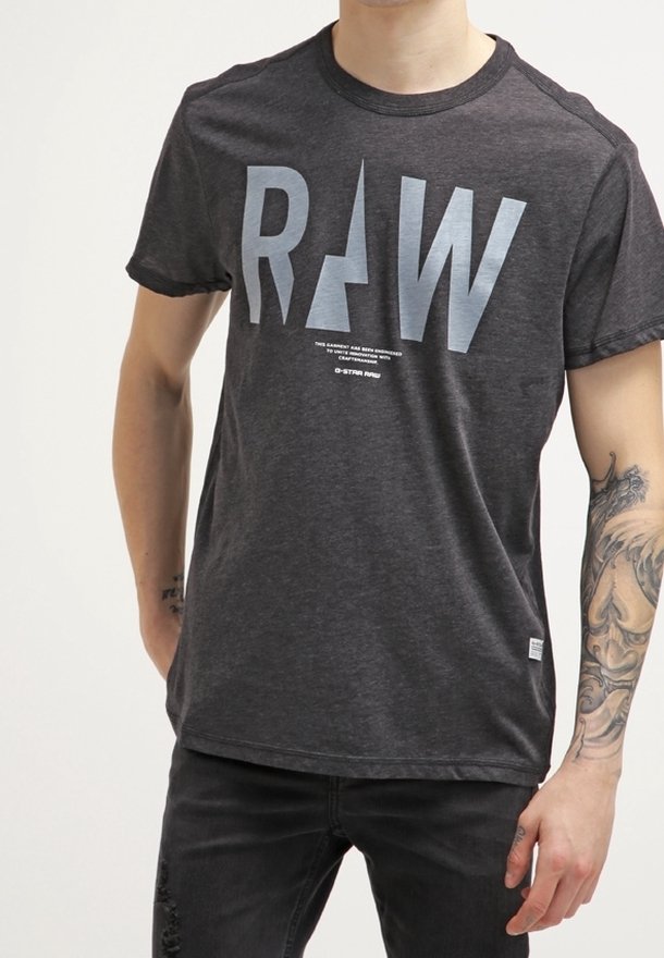 T-shirt gris à manches courtes avec un grand texte "RAW" en bleu clair, col rond et texture en coton doux. Associé à un jeans foncé.