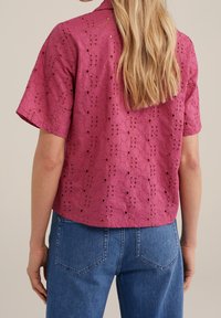 Rosa kortärmad skjorta med broderad blommönster och utskärningar, matchad med blå högmidjade jeans i rak modell.