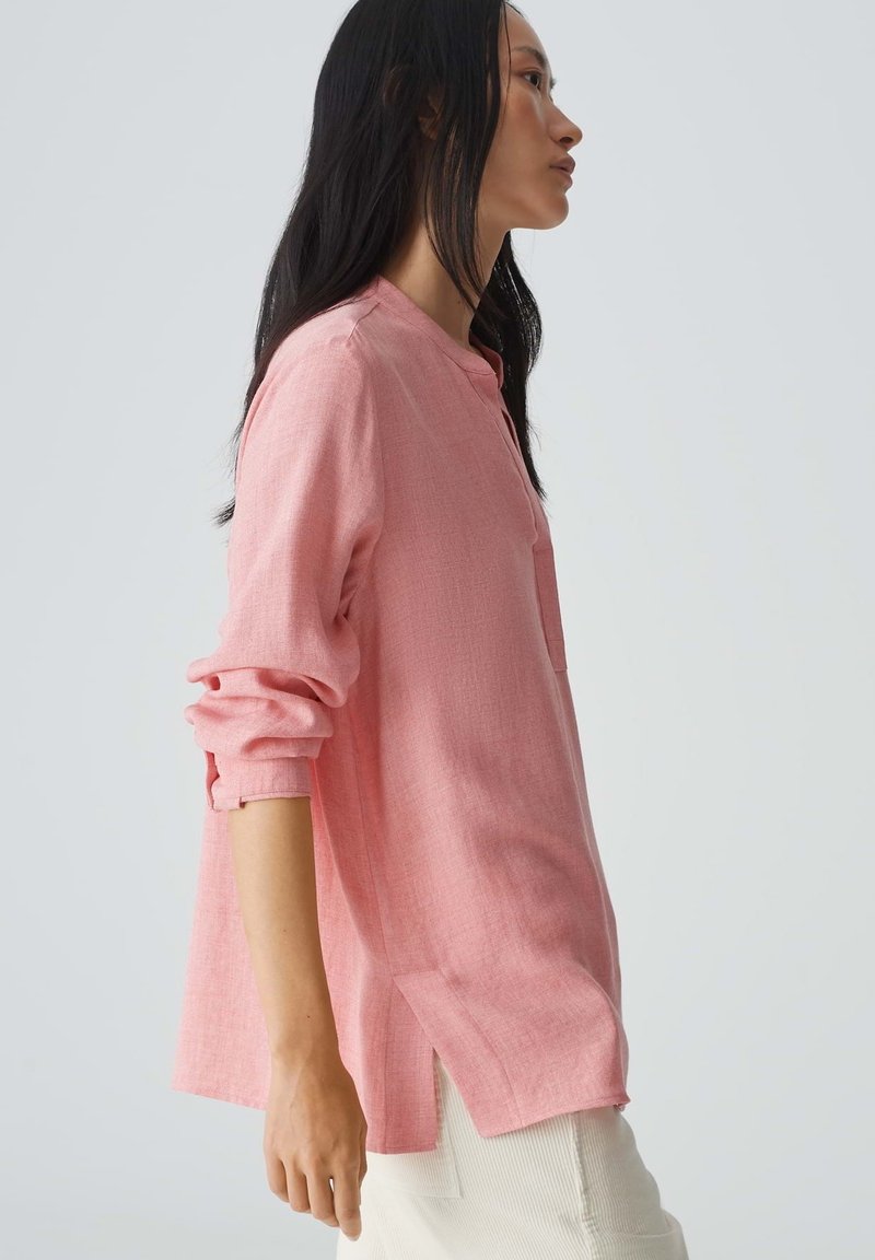 Helles, rosa, strukturiertes Langarmshirt mit Kragen und seitlichen Schlitzen, das eine lockere Passform und hochgekrempelte Ärmel aufweist.