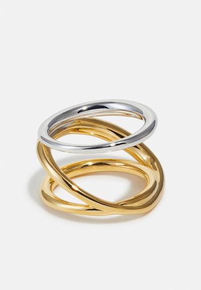 Trois anneaux métalliques lisses entrelacés, deux dorés et un argenté, disposés dans un motif torsadé et superposé sur fond blanc.