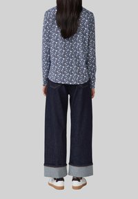 Langärmlige gemusterte Bluse in Marineblau und Weiß, kombiniert mit weit geschnittenen, dunkelblauen Jeans mit hellblauen Manschetten. Weiße Sneakers mit schwarzen Akzenten.
