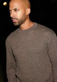 Knitted brown sweater with a textured pattern, round neckline, and fitted sleeves, showcasing a casual design.