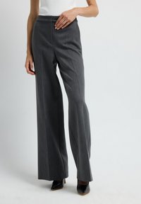 Pantalones anchos grises hechos de una tela texturizada, con una cintura alta y sutiles rayas verticales, combinados con tacones negros de punta.