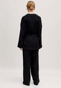 Schwarzes, strukturiertes Outfit mit einem lässigen Oberteil und weit geschnittenen Hosen. Das Oberteil hat einen runden Ausschnitt und ein gebundenes Taillendetail.