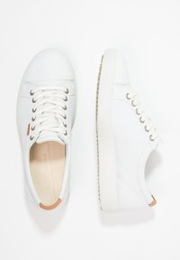 Zapatillas deportivas bajas de cuero blanco con cordones blancos, ojales de metal y pestañas en el talón de color marrón claro, mostradas desde vistas superior y lateral.