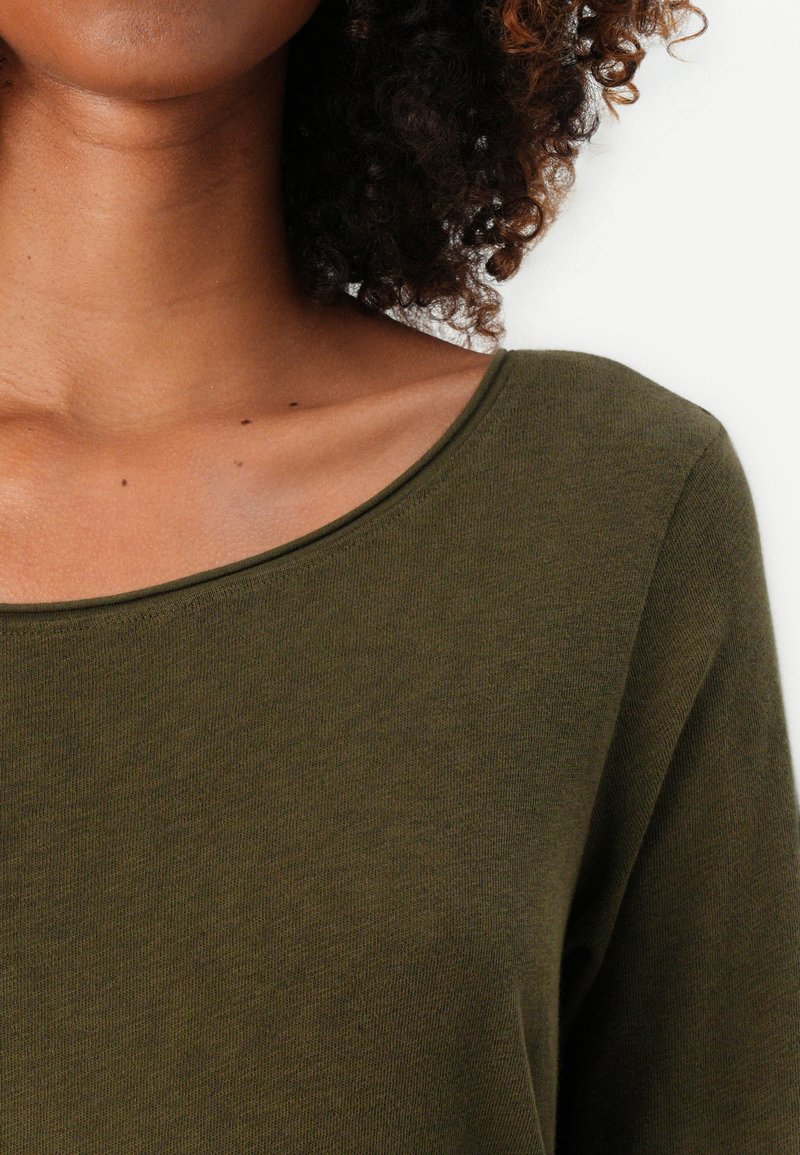 Oliwkowy sweter z szerokim, okrągłym dekoltem i długimi rękawami. Materiał wydaje się miękki o gładkiej fakturze.