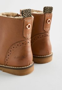 Bruine leren laarzen met een textuur bovenwerk, faux-fur voering, geweven accenten bij de kraag en geperforeerde details aan de zijkanten.