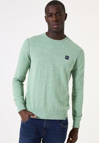 Groene pullover trui met een ronde hals, ribgebreide mouwen en onderrand. Beschikt over een klein marineblauw logo-opdruk op de borst. Textured breiwerk.