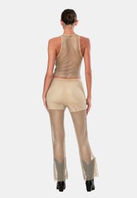 Set composto da top corto in rete dorata e pantaloni a palazzo, caratterizzato da una texture trasparente, un design aderente e un motivo a tessitura aperta, abbinato a stivali platform neri.