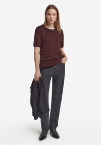 Vinröd kortärmad tröja med rund halsringning, kombinerad med mörkgrå raka byxor och svarta spetsiga skor, håller en svart jacka.