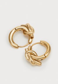 Boucles d'oreilles en or en forme de créoles avec un design noué à l'avant. Forme ronde, texture lisse et finition brillante avec un fermoir à charnière.