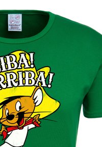 Green short-sleeve T-shirt featuring a cartoon character with a large yellow hat, red neckerchief, and graphic text "Arriba!" in bold black and white.