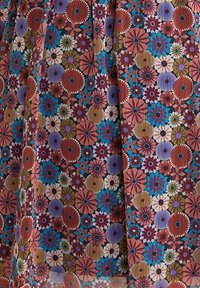 Motif floral en tissu avec des fleurs circulaires qui se chevauchent dans des nuances de rouille, bleu, violet, beige et blanc sur un fond texturé.