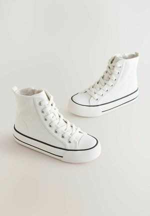 Zapatillas altas de lona blancas con suela de goma, raya negra y diseño de cordones en la parte delantera. Punta texturizada y tira en el talón.