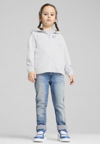 Felpa con zip grigia chiara, jeans blu e sneakers blu. La felpa presenta una piccola grafica. I jeans hanno un leggero effetto lavato.
