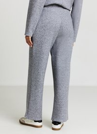 Pantaloni grigi, larghi e comodi, realizzati in un tessuto morbido e dalla texture evidente, con spacchi laterali all'orlo, abbinati a sneakers casual bianche e nere.