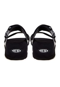 Schwarze Sandalen mit zwei überkreuzten Riemen, strukturiertem Fußbett und schwarzer Gummisohle. Rundes Logo auf der Innensohle. Minimalistisches Design.