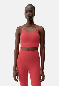 Top corto sportivo rosso con due spalline sottili, tessuto strutturato e design aderente, abbinato a leggings abbinati a vita alta.