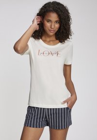 Cremfarbendes T-Shirt mit rundem Halsausschnitt und kurzen Ärmeln, versehen mit einem "LOVE yourself"-Grafikdesign in Pink und Schwarz. Kombiniert mit marineblauen gestreiften Shorts.