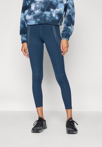 Mørkeblå leggings med en glat tekstur, prydet med prikkede sideaccentuer og en tætsiddende design, parret med en mønstrede sweatshirt og sorte træningssko.