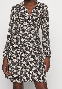 Černé květinové šaty s límečkem, dlouhými rukávy, zapínáním na knoflíky v přední části a kontrastními bílými a oranžovými květinovými vzory.