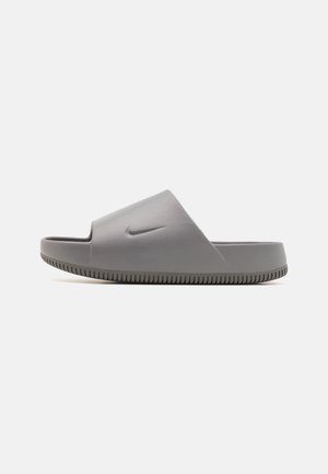 Szary klapek Nike z teksturowaną podeszwą i wytłoczonym logo Swoosh na szerokim pasku, widoczny z boku na białym tle.