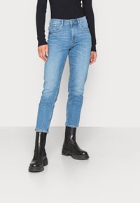 Jeans de denim azul claro con un corte ajustado, diseño de cinco bolsillos y dobladillos enrollados, combinados con botas de tobillo negras de tacón grueso.