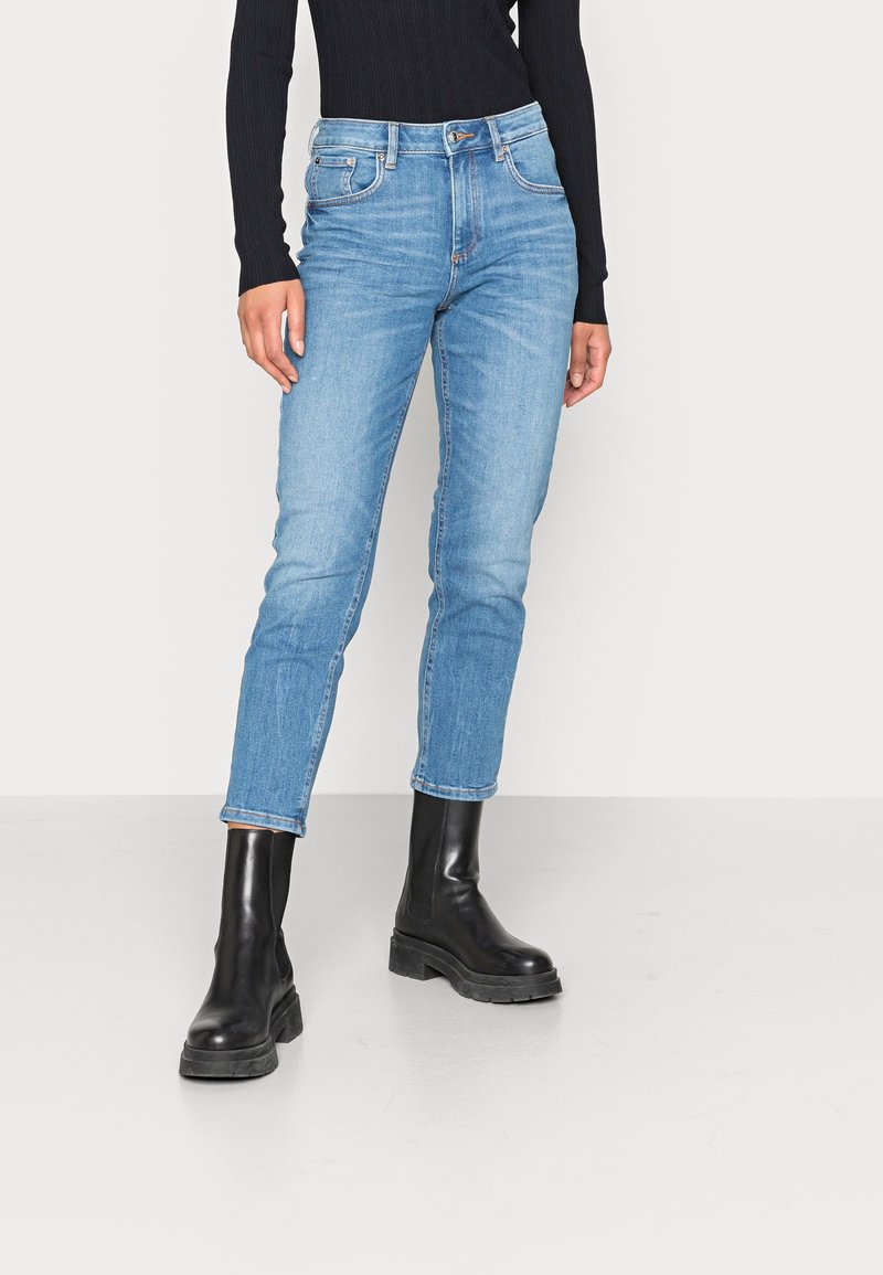 Jeans de denim azul claro con un corte ajustado, diseño de cinco bolsillos y dobladillos enrollados, combinados con botas de tobillo negras de tacón grueso.