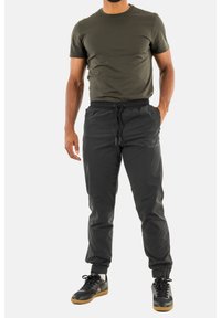 Schwarze Sporthose mit elastischem Bund, Kordelzug und schmal zulaufendem Bein, kombiniert mit einem olivgrünen Rundhalsausschnitt-T-Shirt.