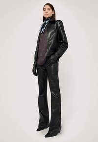 Černá kožená bunda a kalhoty, přiléhavý střih. Modelka má na sobě vzorovanou blůzu a modrý hedvábný šátek, doplněné černými koženými rukavicemi.