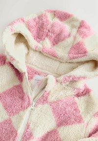 Salopetă cu glugă din fleece, cu un model în carouri roz și crem, cu închidere cu fermoar și textură moale. Interiorul este căptușit cu un material crem asortat.