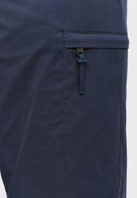 Marineblauwe stoffen shorts met een ritszak en een getextureerd oppervlak. De zak heeft een blauwe ritsenlip met merktekst.