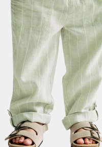 Lichtgroene linnen broek met witte verticale strepen, opgerolde zomen, gecombineerd met beige sandaal met een band en een stevige zool.