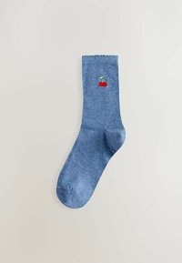 Blauer Socke mit gewelltem Rand und gesticktem Motiv von zwei roten Kirschen an der Seite, auf hellem Hintergrund.