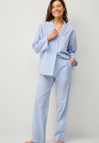 Blauw-wit gestreepte pyjama set met lange mouwen, knoopsluiting op het shirt en bijpassende broek. Zachte stof met een relaxte pasvorm en borstzak.