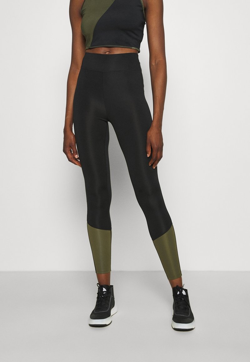Completo sportivo nero e verde oliva composto da un top corto con design asimmetrico e leggings a vita alta con accenti a blocchi di colore.