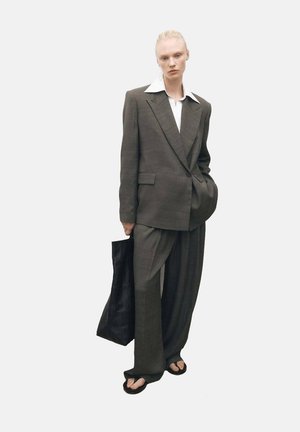 Oversized gray suit with wide-legged trousers, white shirt underneath, and black tote bag. Smooth fabric with a subtle texture.