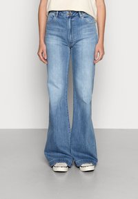 Jeans de ganga azul clara, com corte à boca de sino, de cintura alta, com fecho de botão e cinco bolsos. Tecido texturizado com um acabamento suave.