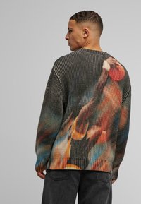Sweter z teksturowanego dzianiny w ciemnych odcieniach, z abstrakcyjnym, wielokolorowym wzorem z tyłu oraz żebrowanym dołem.