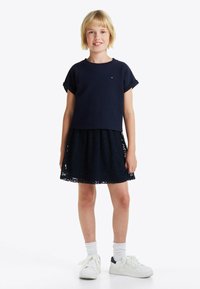 Top de manga corta azul marino combinado con una falda de encaje azul marino, con patrones florales, y zapatillas blancas con toques azul marino, llevadas con calcetines blancos.