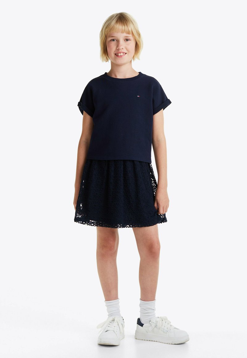 Top de manga corta azul marino combinado con una falda de encaje azul marino, con patrones florales, y zapatillas blancas con toques azul marino, llevadas con calcetines blancos.