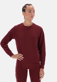 Bordowy sweter z klasycznym dekoltem, długimi rękawami i ściągaczami. Miękka tekstura, minimalistyczny design i dopasowany fason.