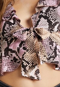 Top con stampa snake in tonalità rosa e marrone, colletto arricciato e dettaglio con fiocco al centro. Tessuto leggero e strutturato.