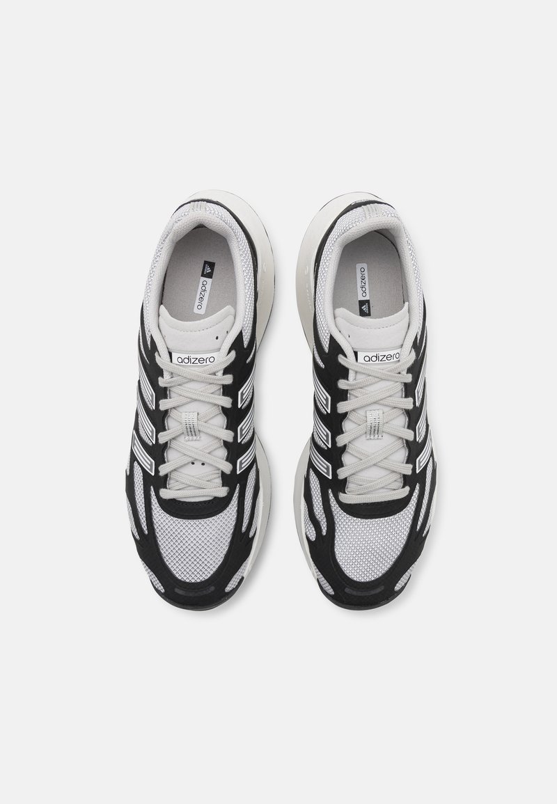 Scarpe da ginnastica in bianco e nero realizzate con materiali in rete e sintetici, caratterizzate da un motivo testurizzato, una tomaia traspirante e un design con lacci.