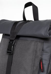 Sac à dos noir à texture roulée avec une surface brillante, des bretelles ajustables et une poche à fermeture éclair latérale avec une accent rouge.