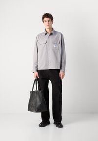 Light gray button-up shirt with two chest pockets, paired with black pants and a black leather tote bag featuring an embossed logo.