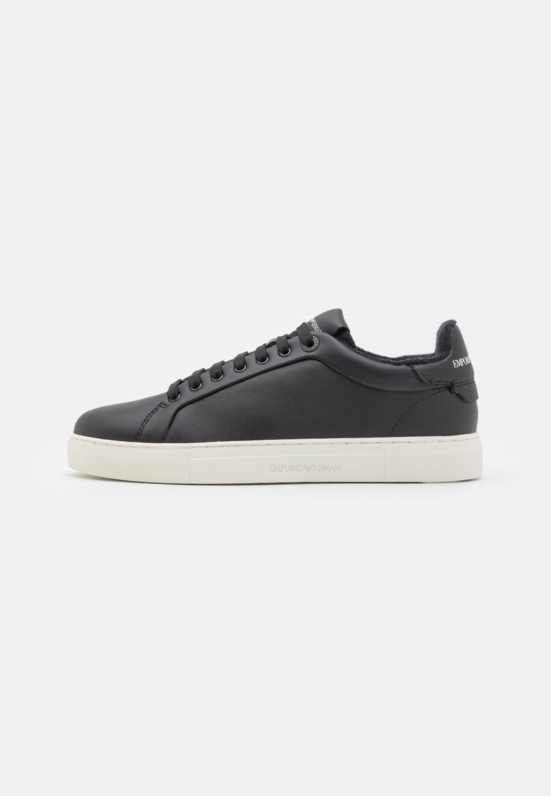 Baskets basses en cuir noir avec lacets noirs, semelle blanche et logo de la marque sur le talon et la semelle sur fond blanc.