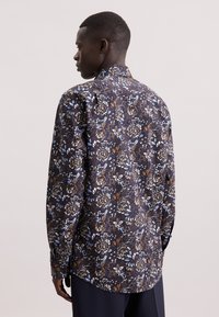 Camicia a maniche lunghe in tessuto blu scuro con un motivo floreale che presenta tonalità di blu, bianco e marrone; colletto diritto e polsini con bottoni.